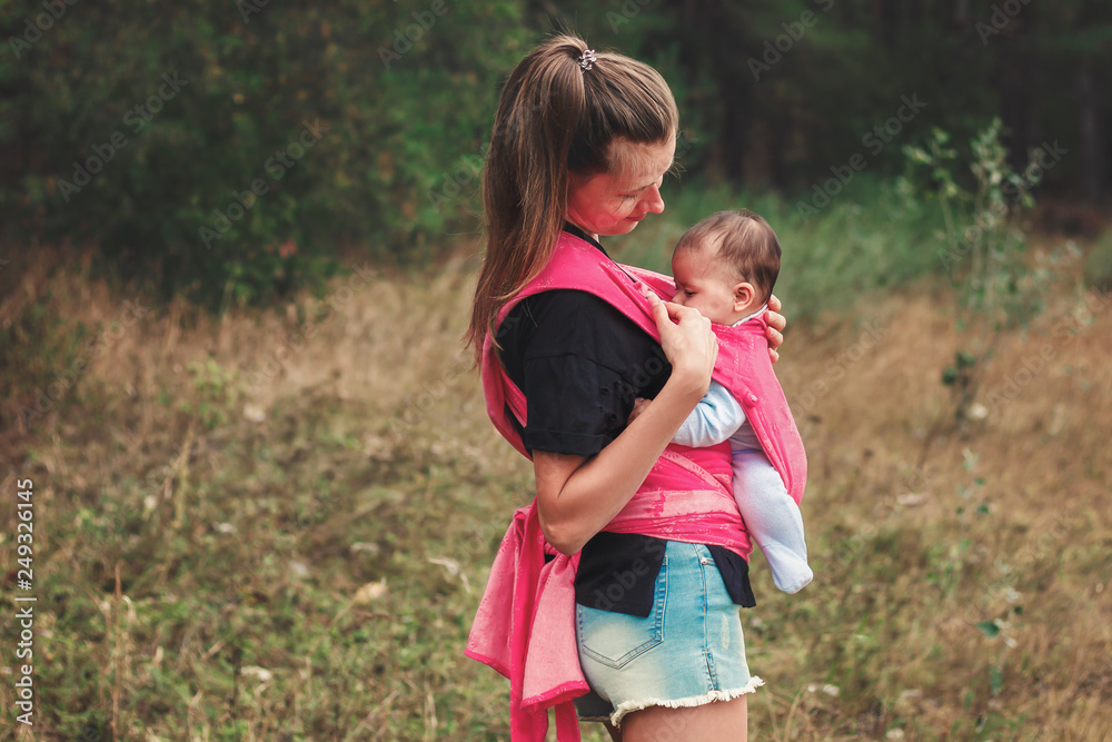 Young mother with a baby in a pink sling. Concept - modern mobile young woman has time for everything Young mother with a baby in a pink sling. Concept - modern mobile young woman has time for everything