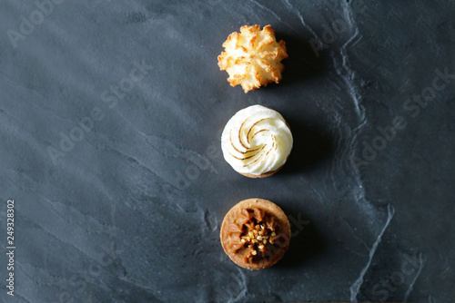 Top view of delicious French mini cakes lined up on black slate with text space