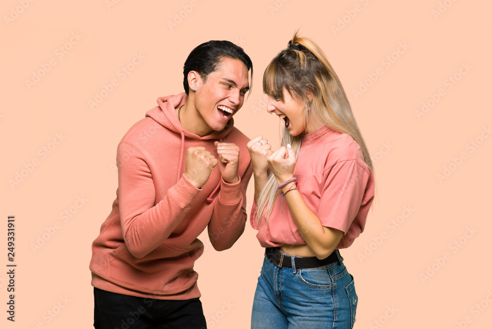 Young couple celebrating a victory in winner position over pink background Young couple celebrating a victory in winner position over pink background