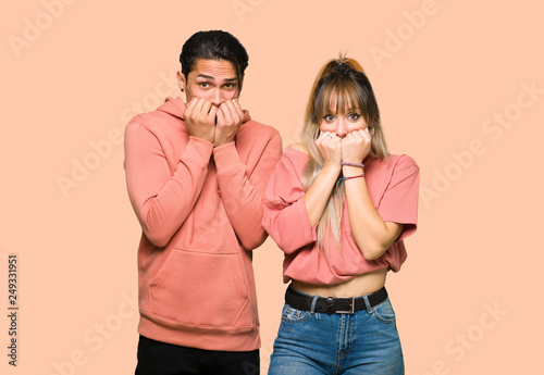 Young couple is a little bit nervous and scared putting hands to mouth over pink background