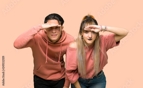 Young couple looking far away with hand to look something over pink background