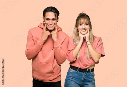 Young couple smiling with a happy and pleasant expression over pink background