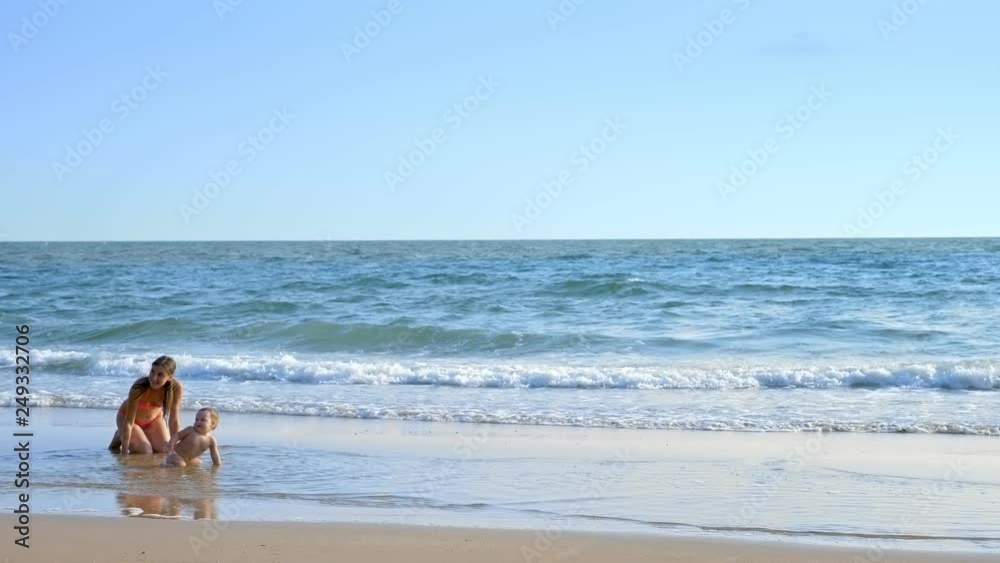 blonde Baby crawling on the sandy beach, mom happily looks at her blonde Baby crawling on the sandy beach, mom happily looks at her
