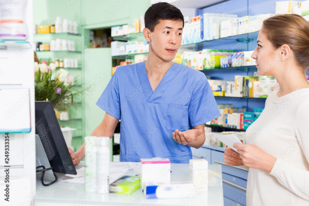 Korean man pharmacist is recommending medicine for young woman client near cashbox in apothecary.