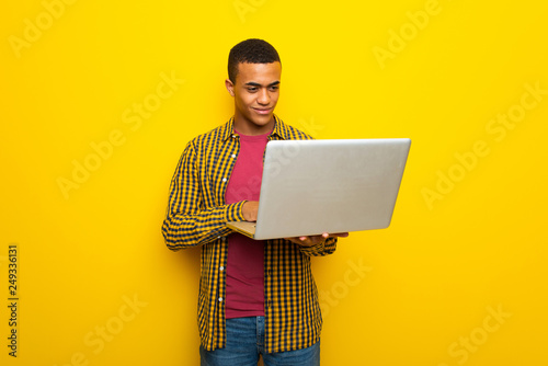 Young afro american man on yellow background with laptop