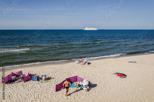 REST ON THE SEA BEACH - People on golden sand and a cruise passenger ship on the sea