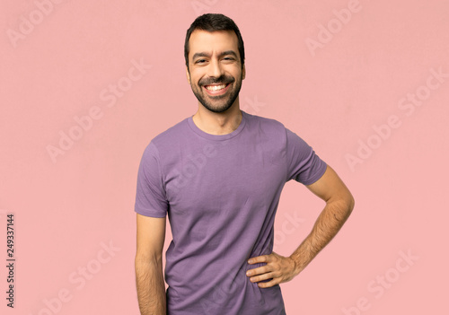Handsome man posing with arms at hip and smiling on isolated pink background