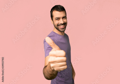 Handsome man giving a thumbs up gesture because something good has happened on isolated pink background