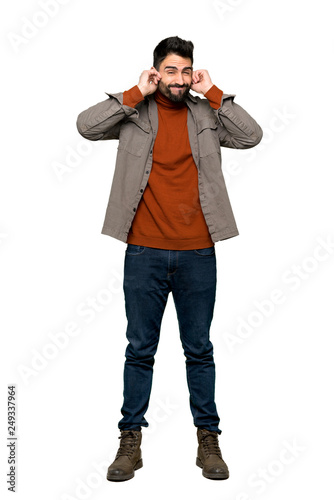 Full-length shot of Handsome man with beard covering ears with hands. Frustrated expression on isolated white background