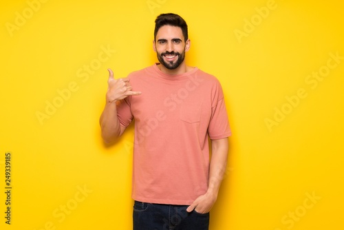 Handsome man over yellow wall making phone gesture. Call me back sign