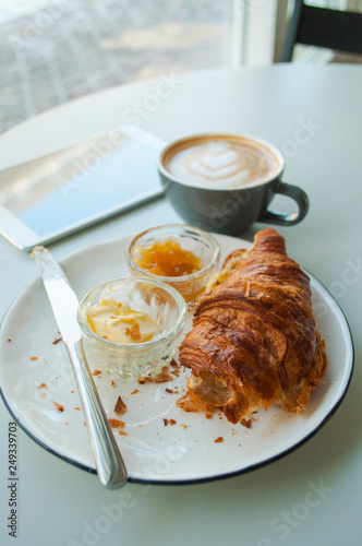 Delicious fresh breakfast. Fresh croissant with jam and butter and a cup of cappucino.