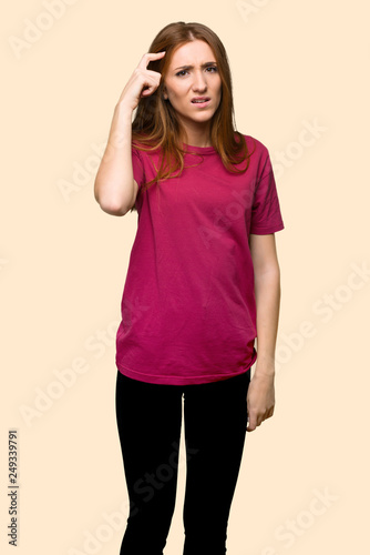 Young redhead girl making the gesture of madness putting finger on the head on isolated yellow background