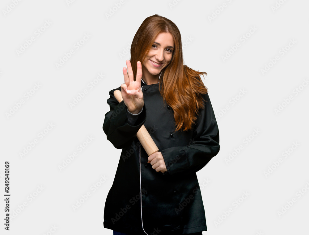 Young redhead chef woman happy and counting three with fingers on isolated grey background Young redhead chef woman happy and counting three with fingers on isolated grey background