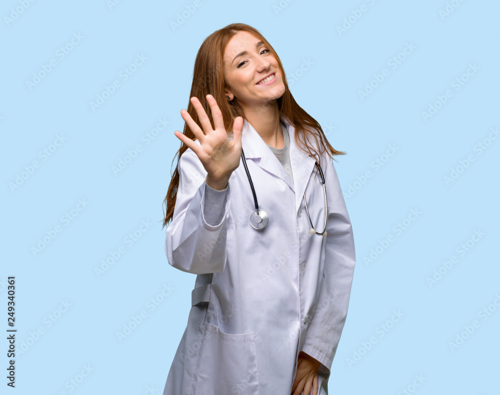 Redhead doctor woman counting five with fingers on isolated blue background Redhead doctor woman counting five with fingers on isolated blue background