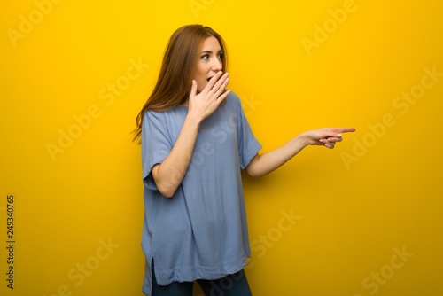 Young redhead girl over yellow wall background pointing finger to the side with a surprised face