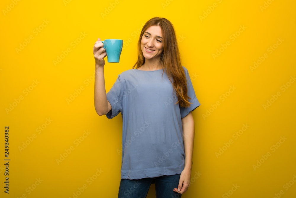 Young redhead girl over yellow wall background holding a hot cup of coffee Young redhead girl over yellow wall background holding a hot cup of coffee