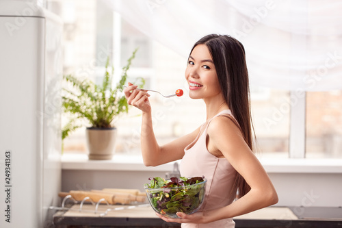 Young girl at kitchen healthy lifestyle walking with bowl and tomato on fork looking back playful