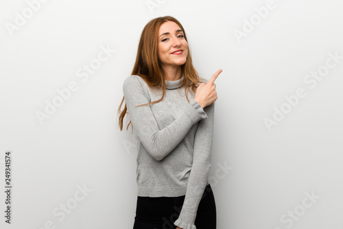 Redhead girl over white wall pointing to the side to present a product