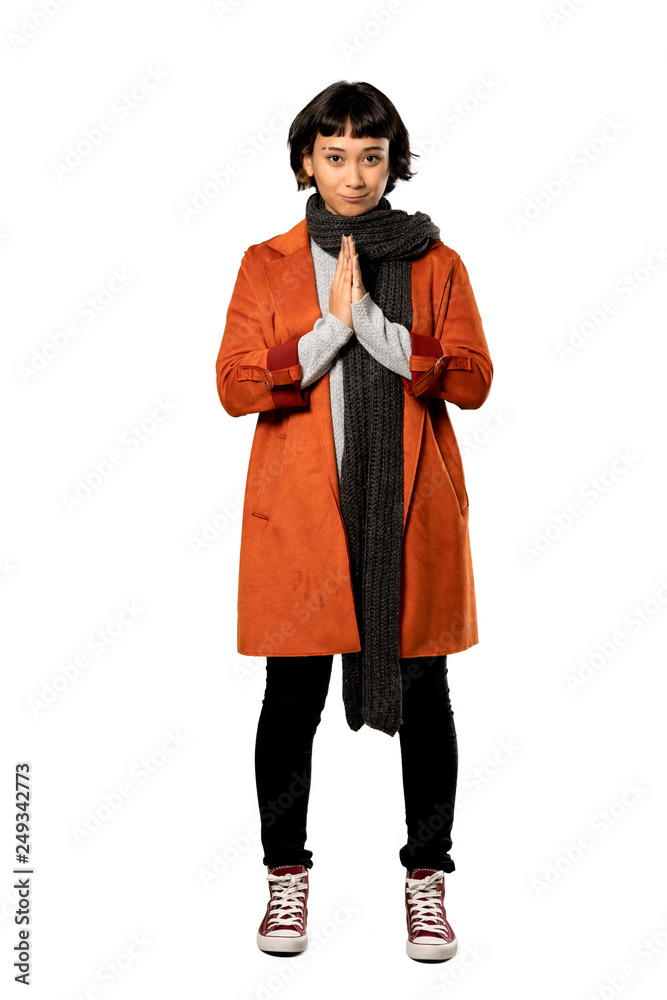 A full-length shot of a Short hair woman with coat keeps palm together. Person asks for something over isolated white background