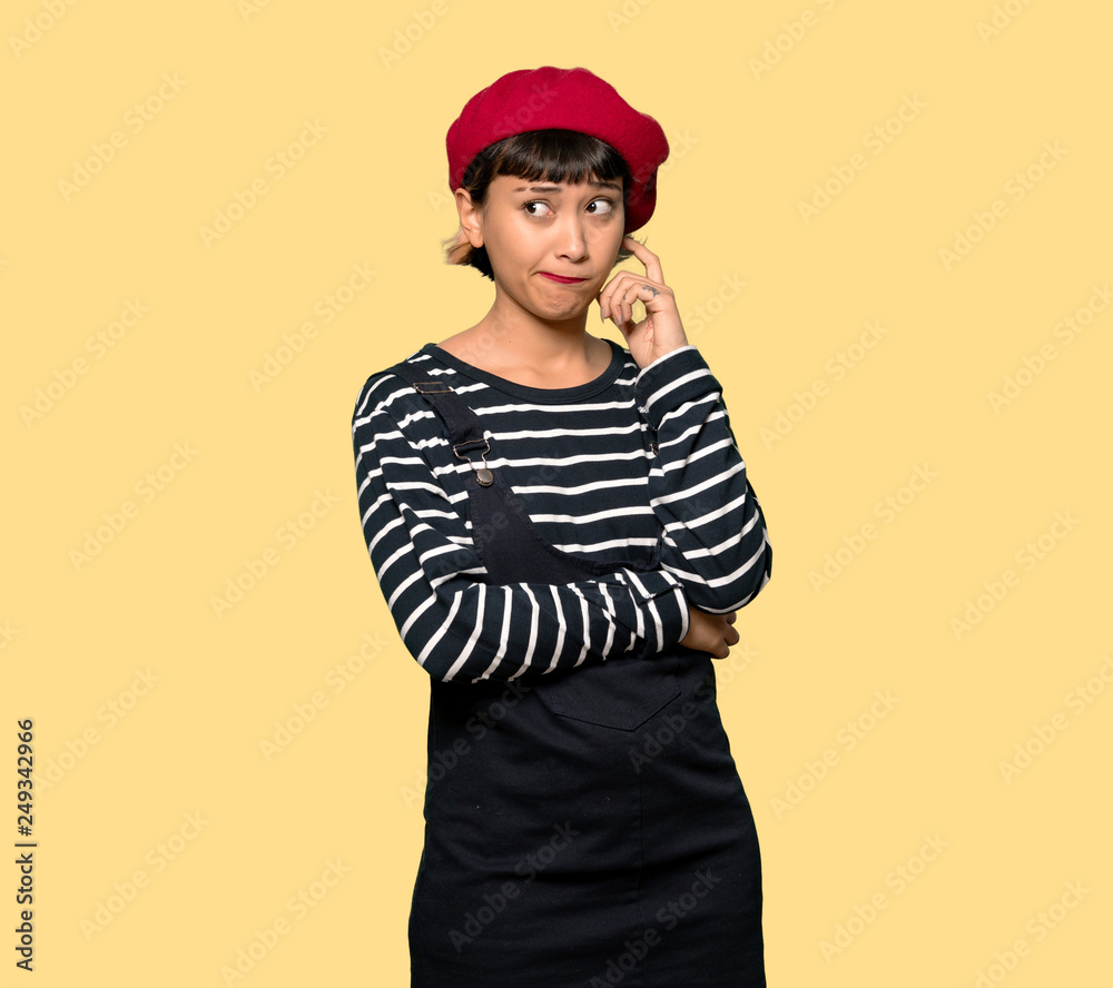 Young woman with beret with confuse face expression while bites lip over yellow background Young woman with beret with confuse face expression while bites lip over yellow background