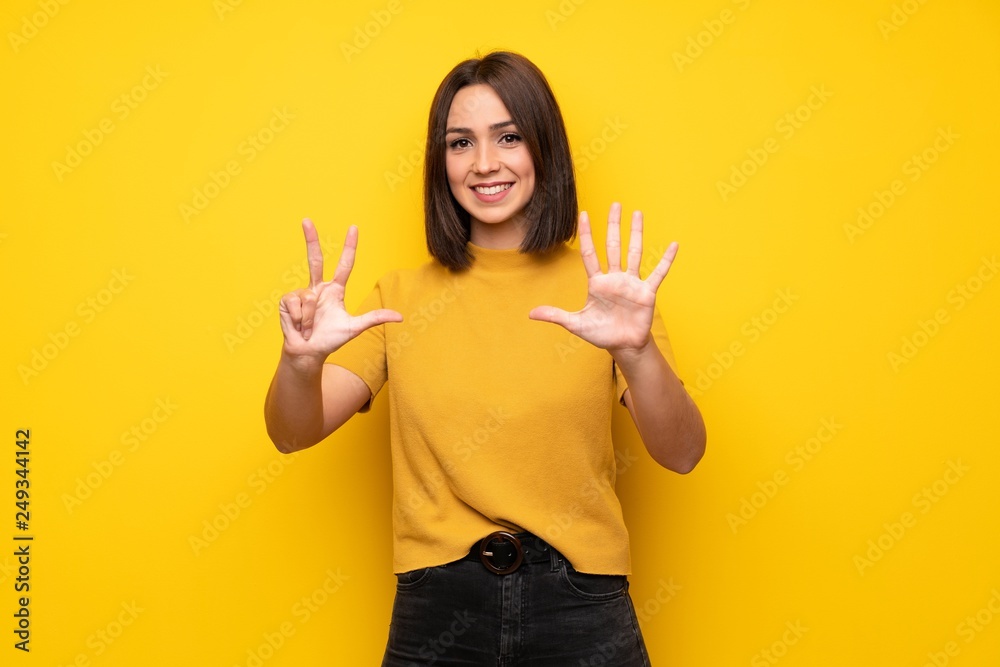 Young woman over yellow wall counting eight with fingers Young woman over yellow wall counting eight with fingers