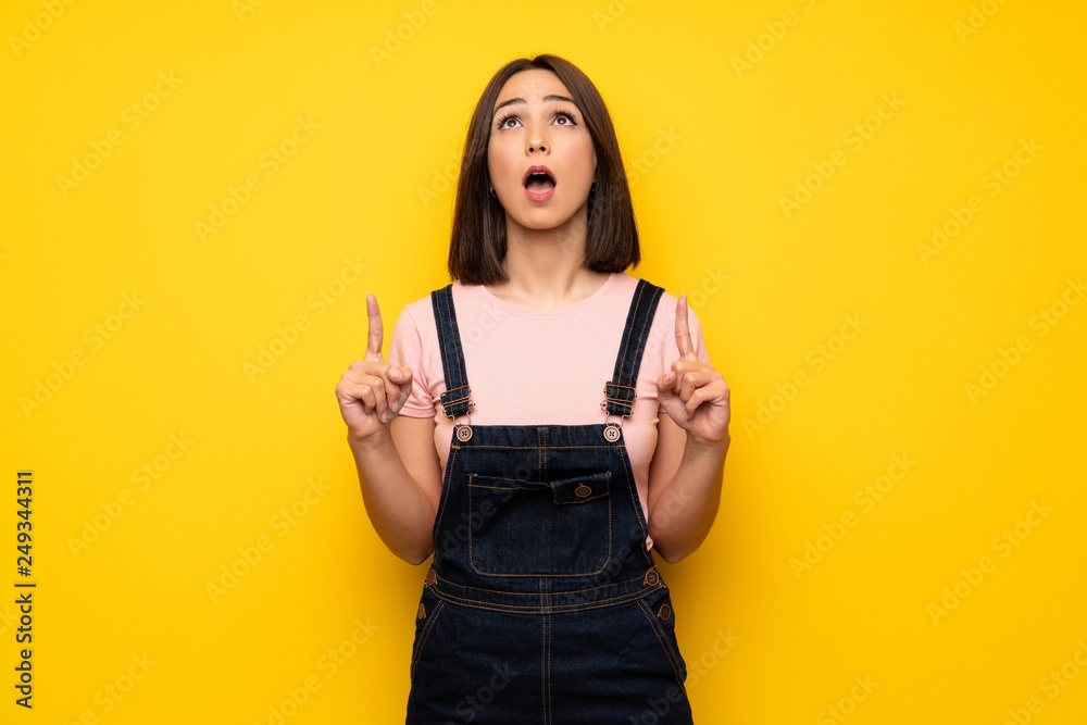 Young woman over yellow wall surprised and pointing up Young woman over yellow wall surprised and pointing up