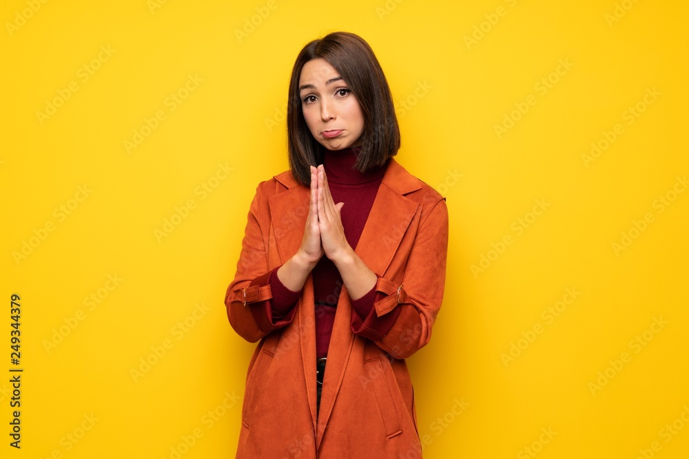 Young woman with coat keeps palm together. Person asks for something Young woman with coat keeps palm together. Person asks for something
