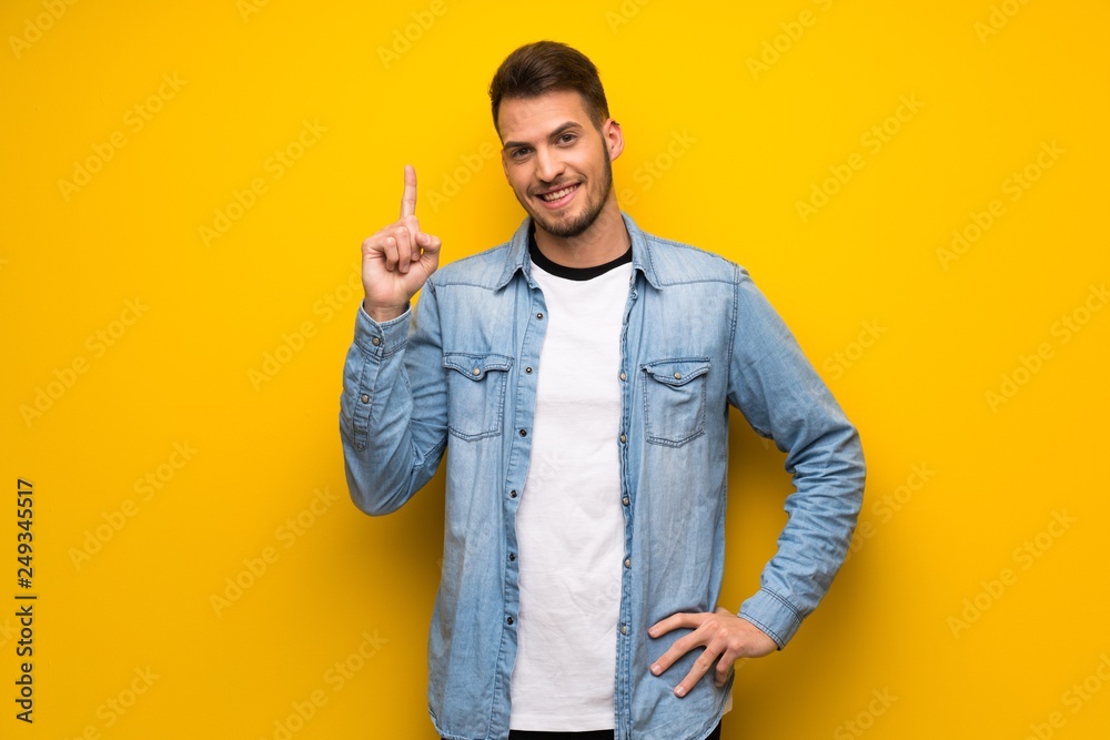Handsome man over yellow wall showing and lifting a finger in sign of the best Handsome man over yellow wall showing and lifting a finger in sign of the best