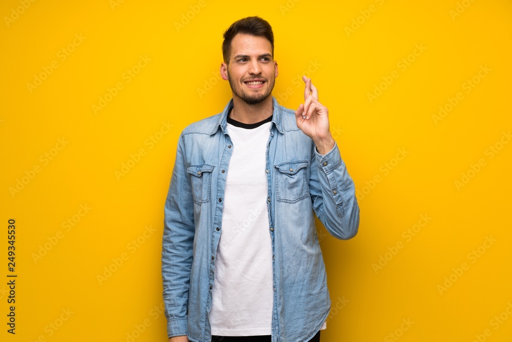 Handsome man over yellow wall with fingers crossing and wishing the best Handsome man over yellow wall with fingers crossing and wishing the best
