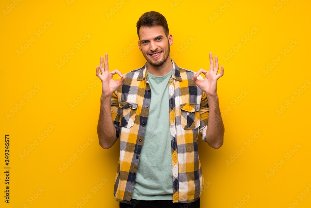 Handsome man over yellow wall showing ok sign with fingers Handsome man over yellow wall showing ok sign with fingers
