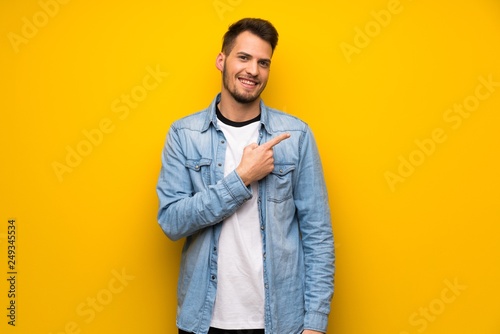Handsome man over yellow wall pointing to the side to present a product © luismolinero