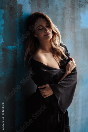 Portrait of beautiful young blonde woman in a silk long dress, fashion and beauty, posing over textured wall background