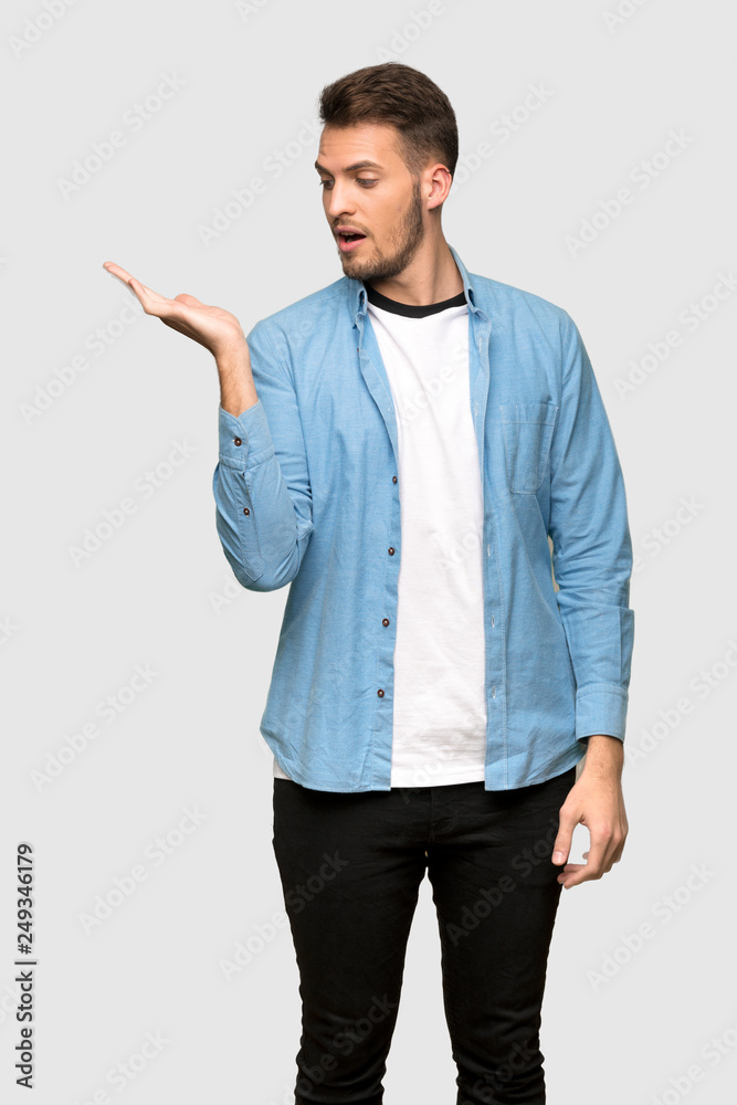 Handsome man holding copyspace imaginary on the palm to insert an ad over grey background
