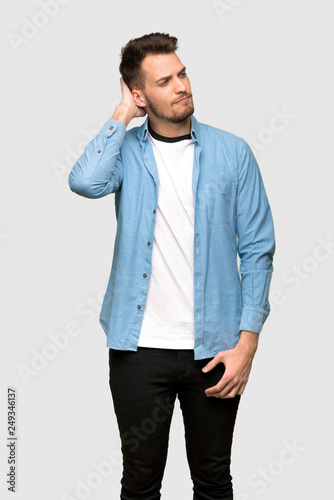 Handsome man having doubts while scratching head over grey background