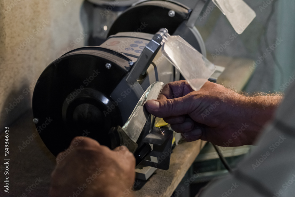 Man sharpens a knife on an electric grindstone Man sharpens a knife on an electric grindstone