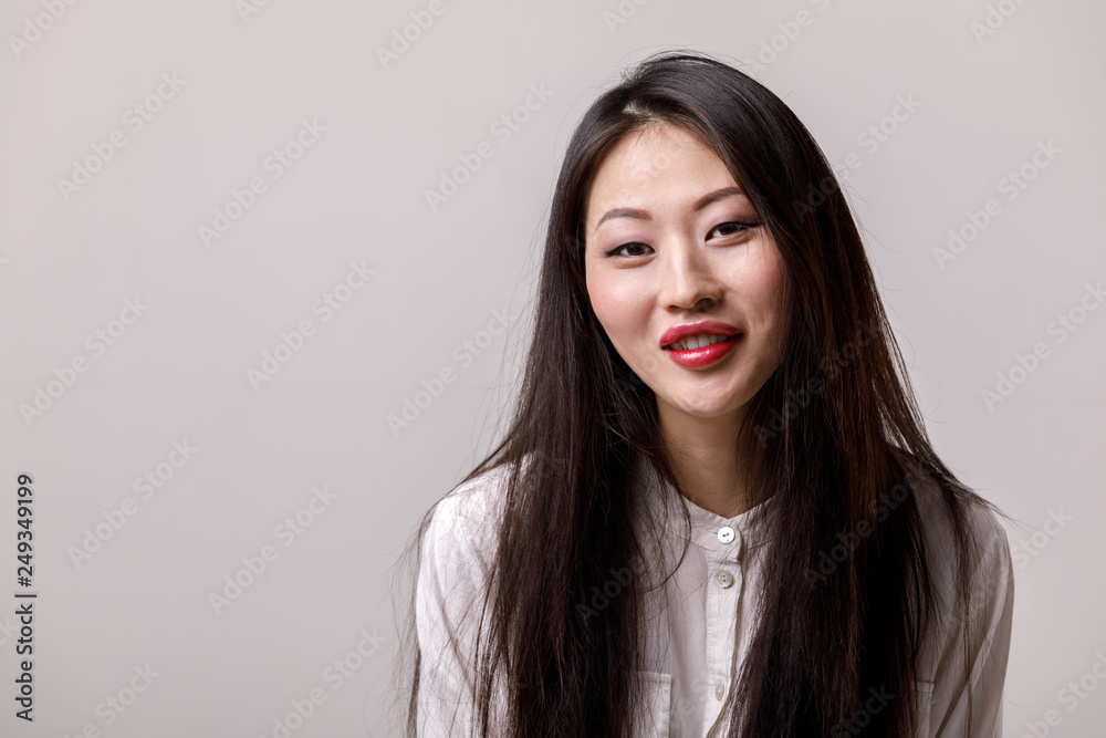 portrait of young smiling asian woman in white shirt on gray background. emotions portrait of young smiling asian woman in white shirt on gray background. emotions