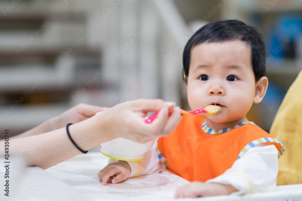 feeding 9 months asian baby girl on high chair. mom feeds blend food to her daughter.Traditional Weaning feeding 9 months asian baby girl on high chair. mom feeds blend food to her daughter.Traditional Weaning