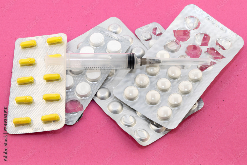 four packs of pills and a syringe on a pink velvet background four packs of pills and a syringe on a pink velvet background