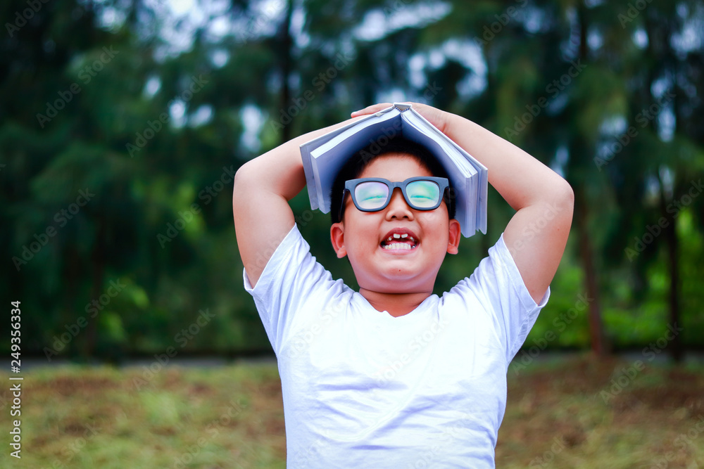 The boy studied elementary, wearing glasses, putting white books on his head.