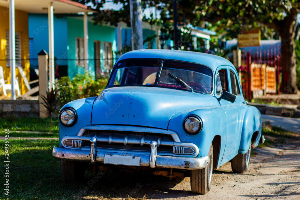 Blue vintage Cuban car parked in front of tropical home in rural Cuba