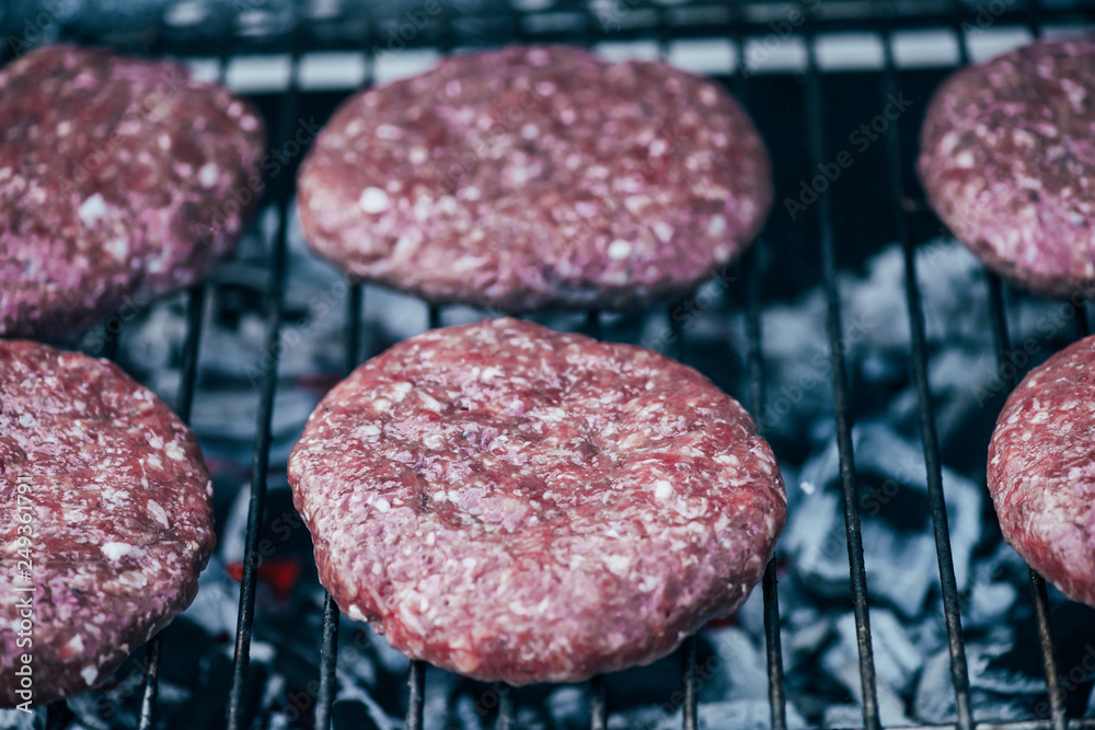 close up of uncooked fresh burger cutlets grilling on bbq grid