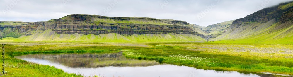 wide angle panorama to little lake and hills in grass in Iceland in summer day