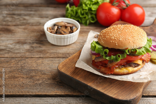 Tasty burger with bacon on wooden board. Space for text