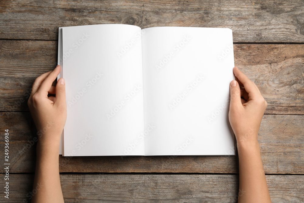 Woman holding brochure with blank pages on wooden background, top view. Mock up for design Woman holding brochure with blank pages on wooden background, top view. Mock up for design