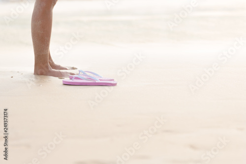 Beach sandals or pink thongs shoes of women on a sandy beach with lots of background copy space.