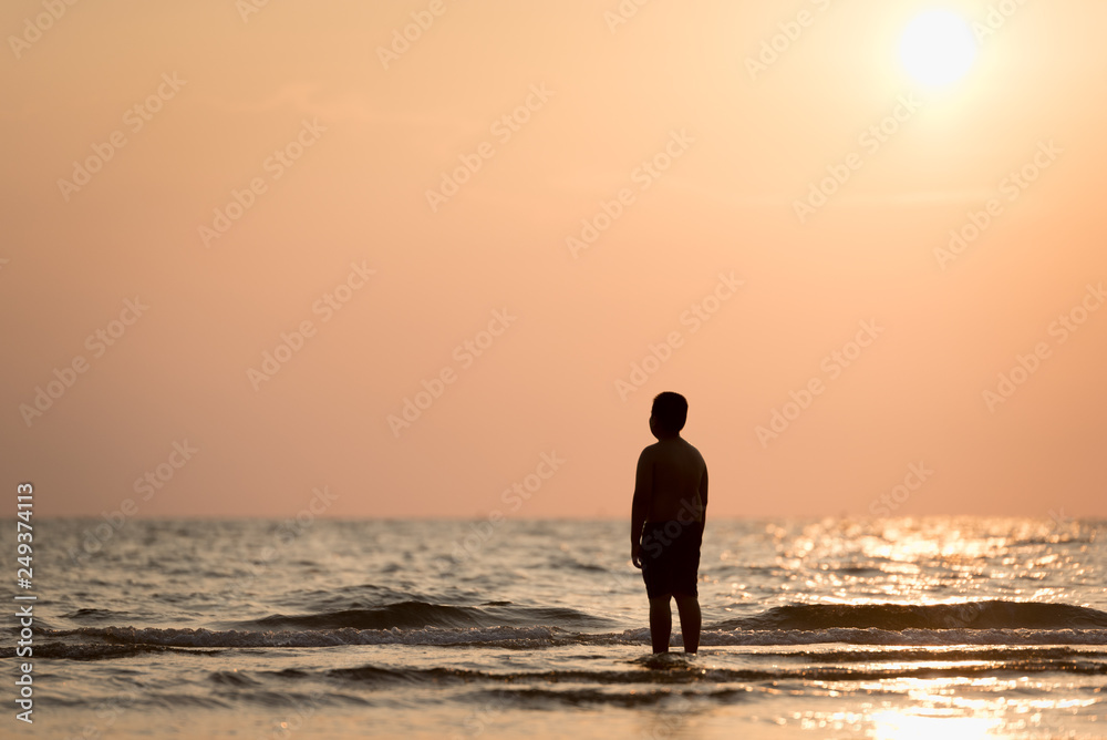 Silhouette of a lonely boy standing alone on the beach at sunset. Concept of lonely and hope of kids or moment of farewell