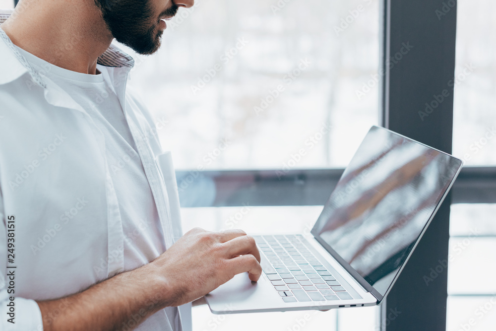 Cropped view of bearded man in white shirt holding laptop Cropped view of bearded man in white shirt holding laptop