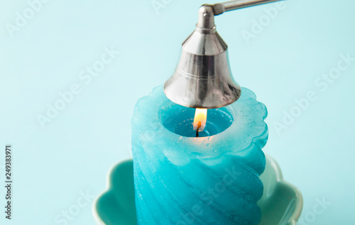 Stainless steel put out candle flame wick long handle candle snuffer bell with lit blue candle on blue studio background. Silver bell on top of flame, about to put out the flame. photo