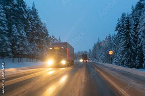 Cars drive with headlights on the winter road in a snow storm in the twilight when snow is flying. Concept of driving in the dangerous conditions with bad visibility on the winter. Image with motion