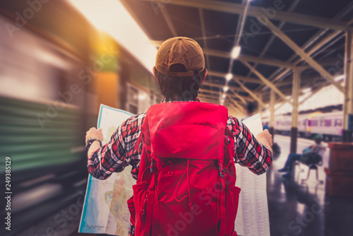 Young man wanderer holding a map and searching direction on location map while traveling train station. Tourist searching location concept. Retro style